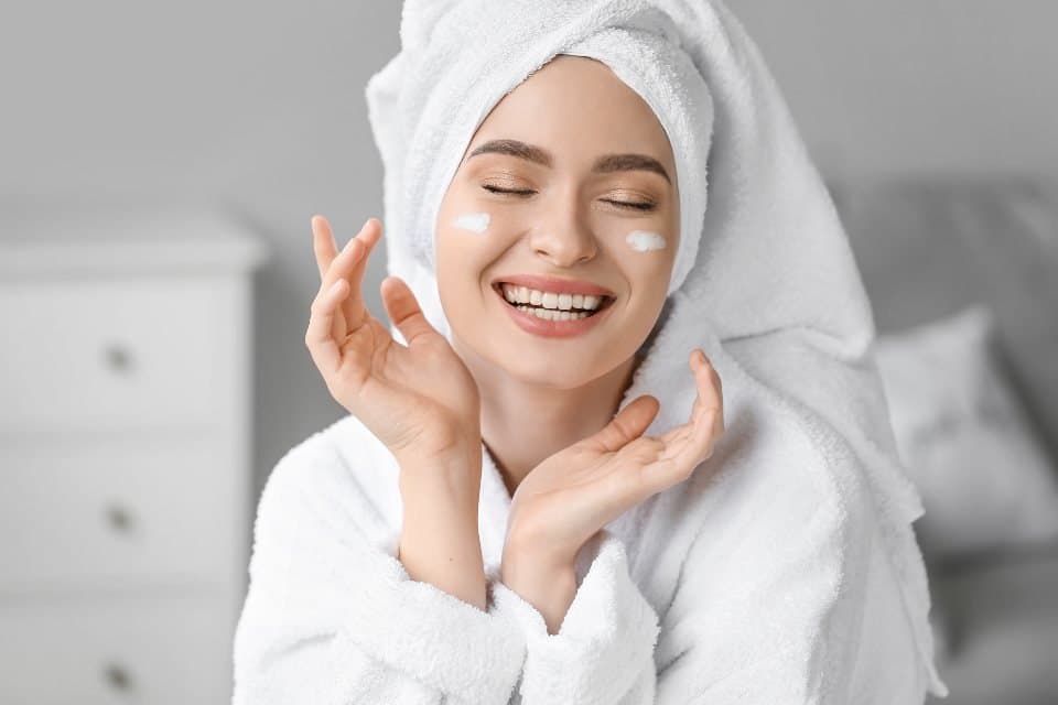 Smiling woman in a towel applying skin cream